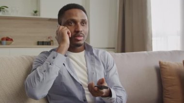 Genç 20 'li yaşlarda Afro-Amerikan bir adam televizyon kumandasını içeride kullanırken kablolu yayın desteği ile sohbet ediyor.