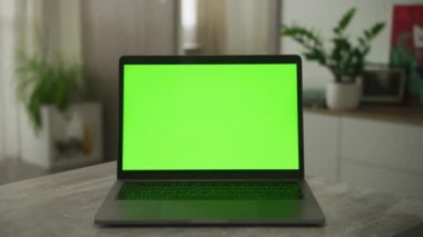 Static video of an open laptop computer with a green screen chroma key on it with a modern apartment in the background