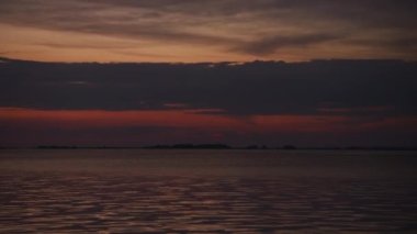Optical zoom out from a sunset clouds over a calm river water in summer