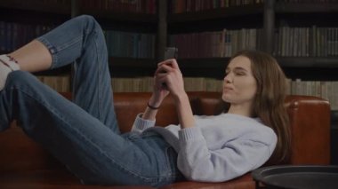 Optical zoom in caucasian woman typing on her smart phone happy and smiling online in slow motion indoors