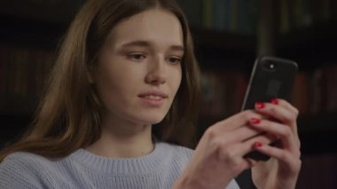 Close up of a caucasian woman texting on her smart phone and laughing in slow motion indoors