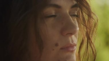 Handheld close up catching sunbeam on curly caucasian woman face with freckles and birthmark outside in slow motion