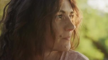 Pivoting around close up portrait of a young adult curly caucasian woman with freckles looking at camera in sunset sunlight in slow motion