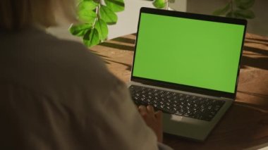 Handheld shot of a woman single scroll on a laptop computer with green screen chroma key indoors in slow motion