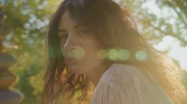 Dreamlike close up portrait of a curly caucasian woman with freckles looking at camera in sunset sunlight with lens flare