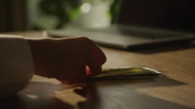 Handheld close up of caucasian woman hands counting money in 100 dollar bills in front of a laptop computer in 90fps slow motion
