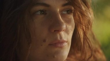 Handheld close up catching sunbeam on curly caucasian woman face with freckles and birthmark outside in slow motion
