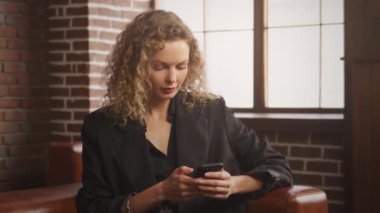 Young 30s business woman is thinking on an answer on a smart phone in a loft apartment indoors
