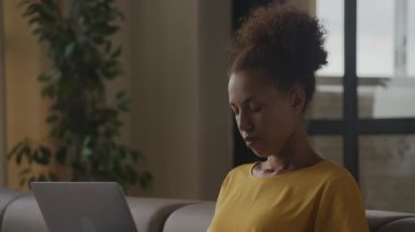 Close up of a young adult African American thoughtful woman thinking on a decision while working on a laptop computer indoors in 90fps slow motion