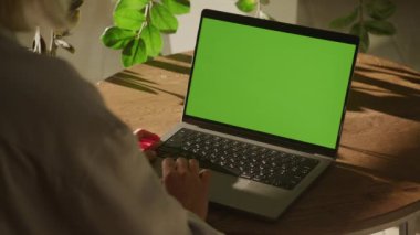 Handheld shot of a woman single scroll on a laptop computer with green screen chroma key indoors in slow motion