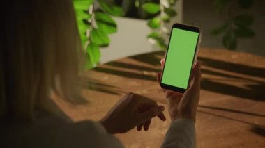 Elinde yeşil ekran krom anahtarı olan akıllı bir telefonu tutan ve 90 fps yavaş çekimde kapalı alanda tek bir geçiş yapan bir kadının el kamerası.