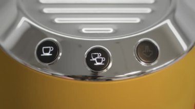 Womans finger pressing the espresso button on a bright yellow coffee machine without makeup