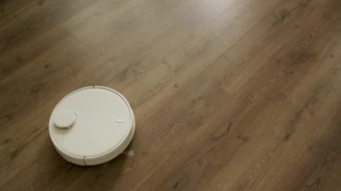 Beyaz elektrikli süpürge robotu, gün ışığında ahşap bir zemin temizliyor.
