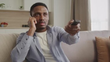 Genç 20 'li yaşlarda Afro-Amerikan bir adam televizyon kumandasını içeride kullanırken kablolu yayın desteği ile sohbet ediyor.