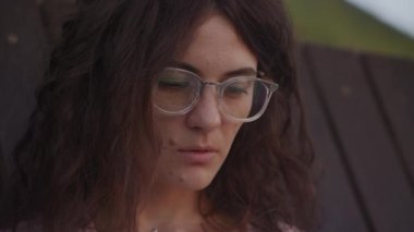Handheld close up of a curly caucasian woman looking at the laptop reflection in her glasses in the park in slow motion