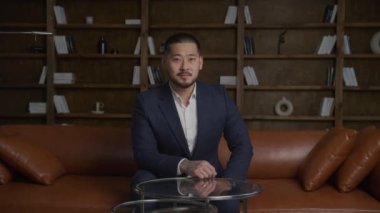 Dövmeli bir Asyalı işadamının portresi kameraya bakıyor ve 75 fps yavaş çekimde çatı katındaki ofiste gülümsüyor.