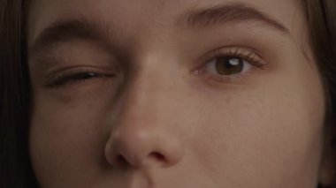 Close up of a caucasian woman eyes in a wink or blink gesture in slow motion indoors