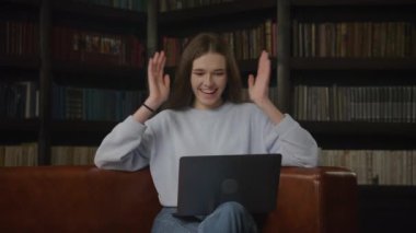 Caucasian student woman waving hand in a greeting gesture on a video call on her laptop indoors