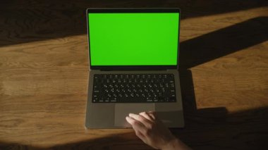 Kafkasyalı bir kadının el kamerası görüntüsü çerçeveye giriyor ve yeşil ekran krom anahtarı olan bir laptopa dokunuyor.