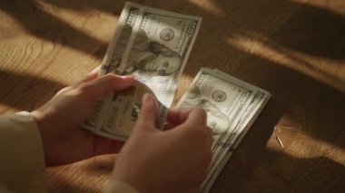 Beyaz bir kadının eli ağır çekimde para sayıyor. 100 dolarlık banknot.