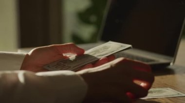 Handheld closee up of caucasian woman hands counting money in front of laptop computer in slow motion