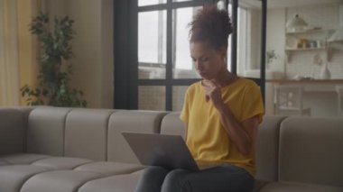 Genç, Afro-Amerikalı bir kadın bilgisayarında internetten alışveriş yaparken neşeli bir ruh hali içinde düşünüyor.