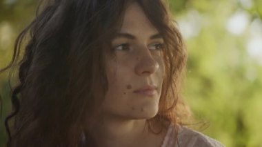 Close up portrait of a young adult curly caucasian woman with freckles looking at sunlight during sunset shot handheld in slow motion