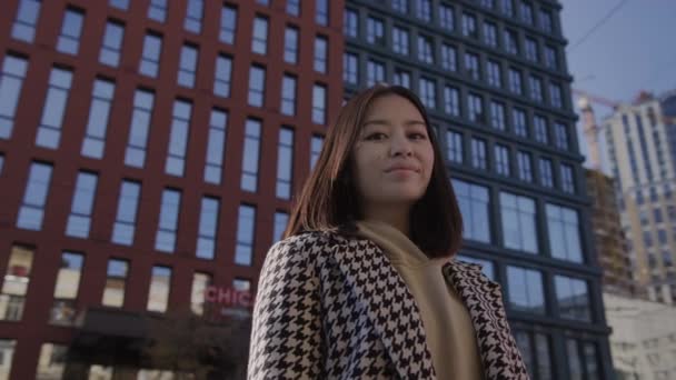 スローモーションで投票する高層ビルの下の都市のダウンタウンのアジアの女性の低角度の肖像画 — ストック動画