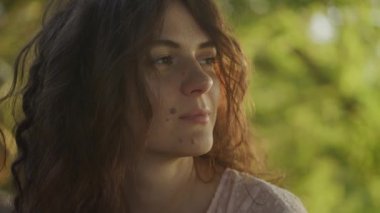 Close up portrait of a young adult curly caucasian woman with freckles looking at sunlight during sunset shot handheld in slow motion
