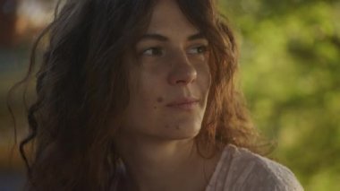 Close up portrait of a young adult curly caucasian woman with freckles looking at sunlight during sunset shot handheld in slow motion