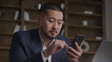 İşadamı Smartphone 'u tarıyor, olumsuz duygu. Dövmeli, takım elbiseli Asyalı adam yüz ifadesinden hoşlanmayan akıllı bir telefonla internette sörf yapıyor.