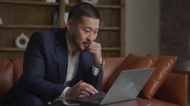 İş adamı çalışıyor. Asyalı Adam Laptop 'a bakıyor. Takım elbiseli yetişkin bir adam, bilgisayarında bir çözüm arıyor. Çatı katındaki ofiste, ağır çekimde.