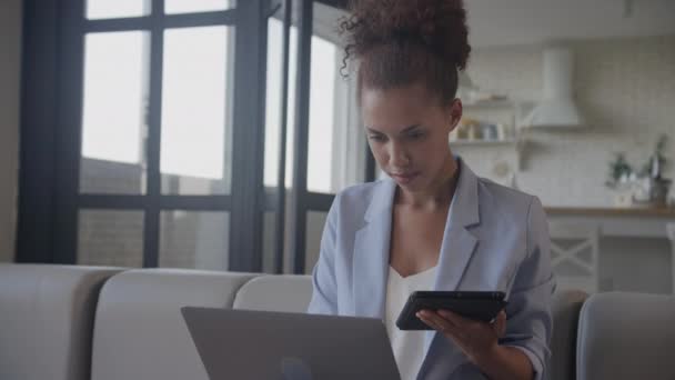 ラップトップコンピュータを使用している間にタブレットで作業するビジネスマン 成人アフリカ系アメリカ人の起業家の女性は 彼女の仕事に近代的な技術を使用して青いスーツ — ストック動画