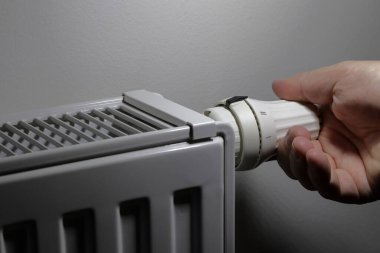 The hand adjusts the radiator valve. Rising energy prices. Heating savings. Photo view from the left. Thermostatic control valve. clipart
