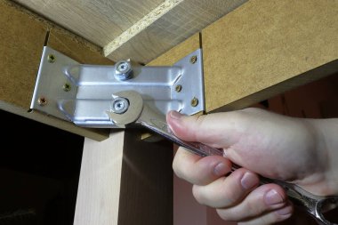 The hand tightens the screw. Hand-operated spanners and wrenches. He repairs the legs of the table.