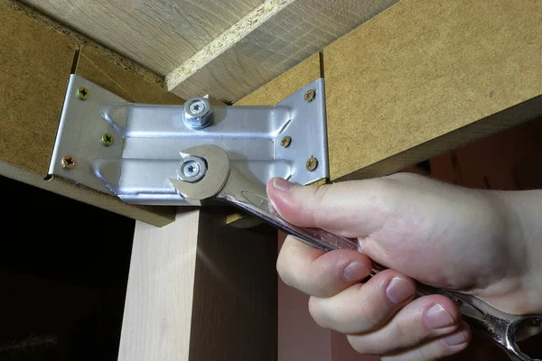 The hand tightens the screw. Hand-operated spanners and wrenches. He repairs the legs of the table.