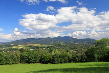 Landscape view of the Beskydy Mountains in the Czech Republic. Blue sky with clouds. Green meadow and forest in the foreground, mountains in the background.