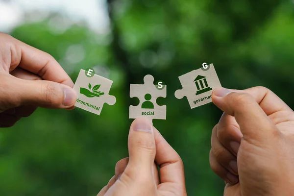 ESG Concepts on Environment, Society and Governance In hand holding puzzle pieces that come together to complete the words ESG and the icon solving environmental problems.