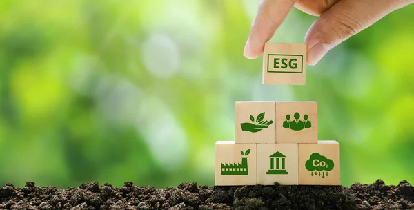 ESG Concepts on Environment, Society and Governance sustainable corporate development Hand holding a wooden cube with ESG abbreviation on a green background.