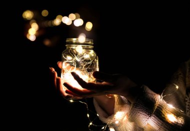 Bir adamın elinde bir ışık, içinde çelenk olan bir kavanozun fotoğrafı ve ışıklardan gelen bir bokeh.