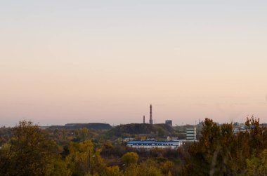 Sonbahar akşamı, güz ağaçları, sanayi binaları, maden, tümsek ve açık gökyüzü olan bir şehir..