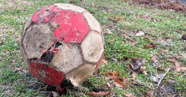 Eski püskü, yırtık bir futbol topu yerde. Gri ve kırmızı. 