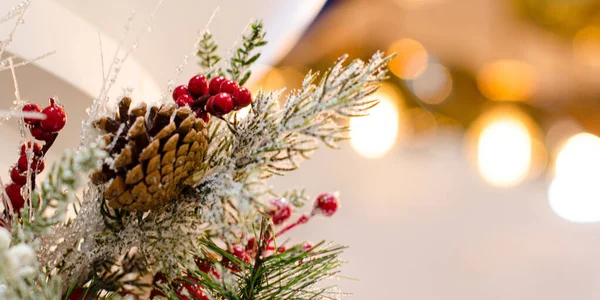 Çam kozalaklı Noel ağacı süslemesi, kırmızı böğürtlen, yapay kar ve altın bokeh ile bulanık arkaplan