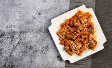 Kare bir tabakta sosisli ve peynirli makarna. Üst manzara, düz uzanma