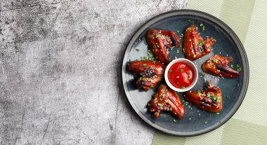 Koyu gri arka planda, yuvarlak tabakta ketçaplı kızarmış tavuk kanadı. Üst manzara, düz uzanma