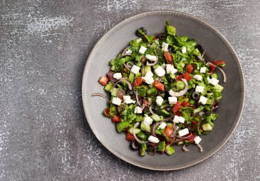 Domatesli salata, salatalık, soğan, marul, zeytin ve koyu arkaplanda yuvarlak tabakta beyaz peynir. Üst manzara, düz uzanma