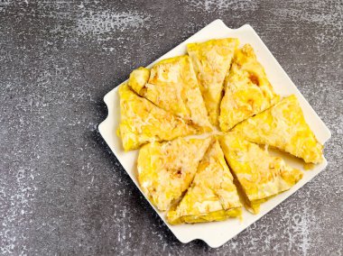 Koyu arkaplanda beyaz dikdörtgen bir tabakta peynirli turta. Üst manzara, düz uzanma