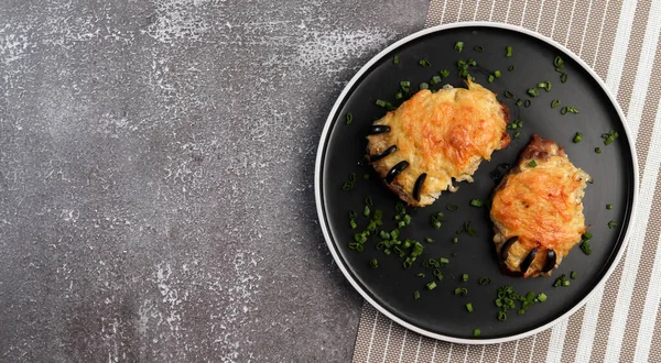 Bear Paw - roasted pork steaks with cheese on a round plate on a dark background. Top view, flat lay