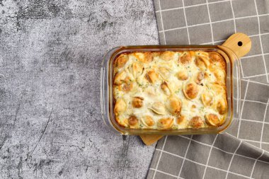 Koyu gri arka planda, cam bir fırında pişirilmiş hamur köftesi güveci. Üst manzara, düz uzanma