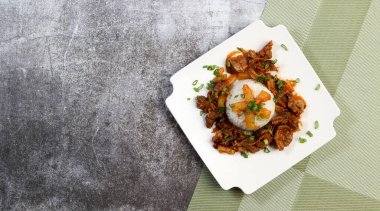Kare bir tabakta kaynamış pirinçli tavuk taşları ve koyu gri bir arka plan. Üst manzara, düz uzanma